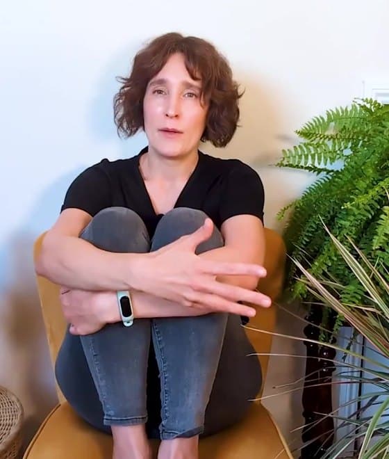 Kristin Loeer sitting curled up in a yellow chair, hugging her knees, showing how the exhausted part can sit in the body.