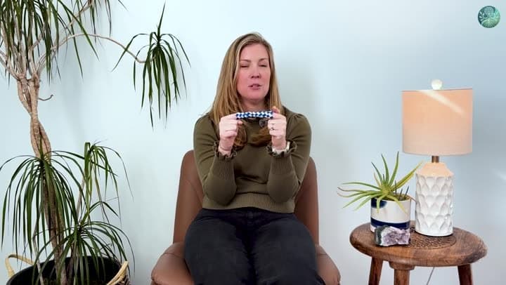 Cate Evans holding up a blue and white Chinese finger trap between her hands.